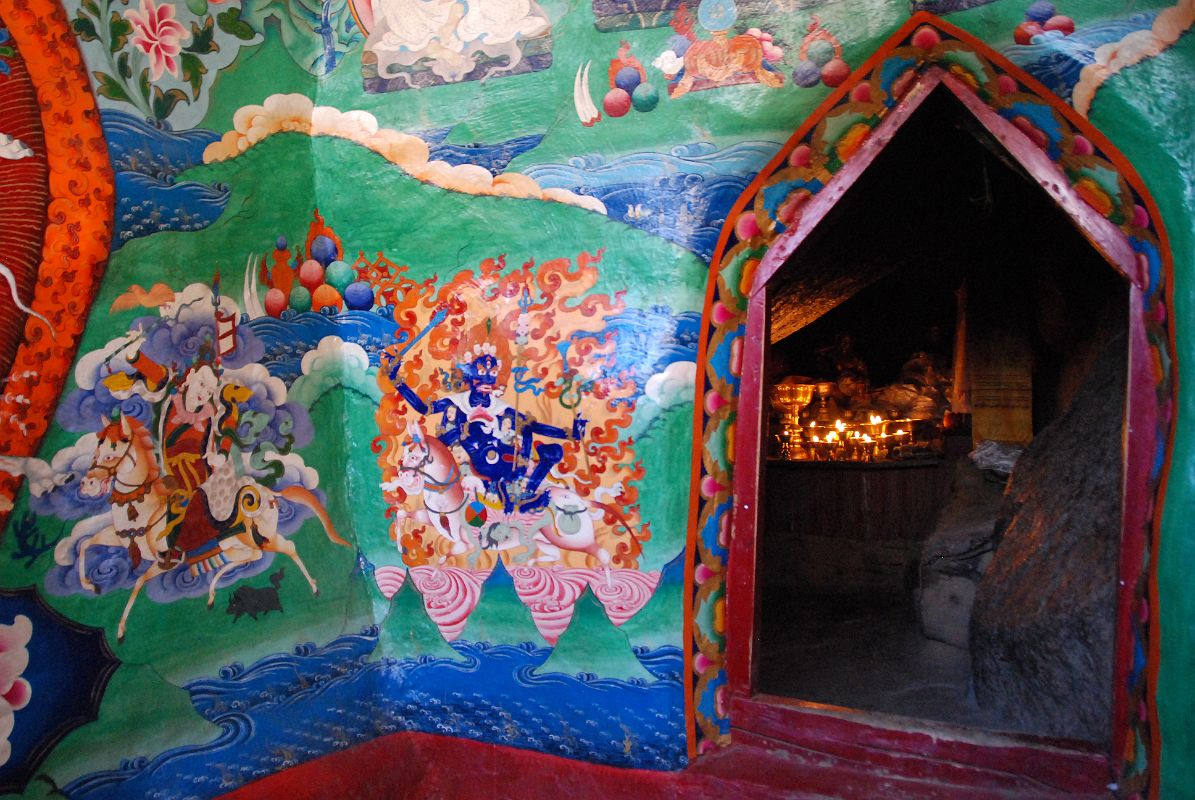 34 Entrance To The Cave Of The Female Yak Horns At The Back Of Dirapuk Gompa On Mount Kailash Outer Kora A small opening at the back of the Dirapuk Gompa leads to the slanted rood of the cave of the female yak horns. Im not sure who the figure is to the left. He is white with one face and two hands holding upraised in the right a riding whip and in the left a spear with a red banner. The final figure to the lower right is Shri Devi (Tib. Palden Lhamo), dark blue in colour, riding side saddle on a white mule with a sword in her upper right, a skullcup in her lower right, and khatvanga in her first right hand and another staff in her far right hand. She has a sun and moon disc at her waist.